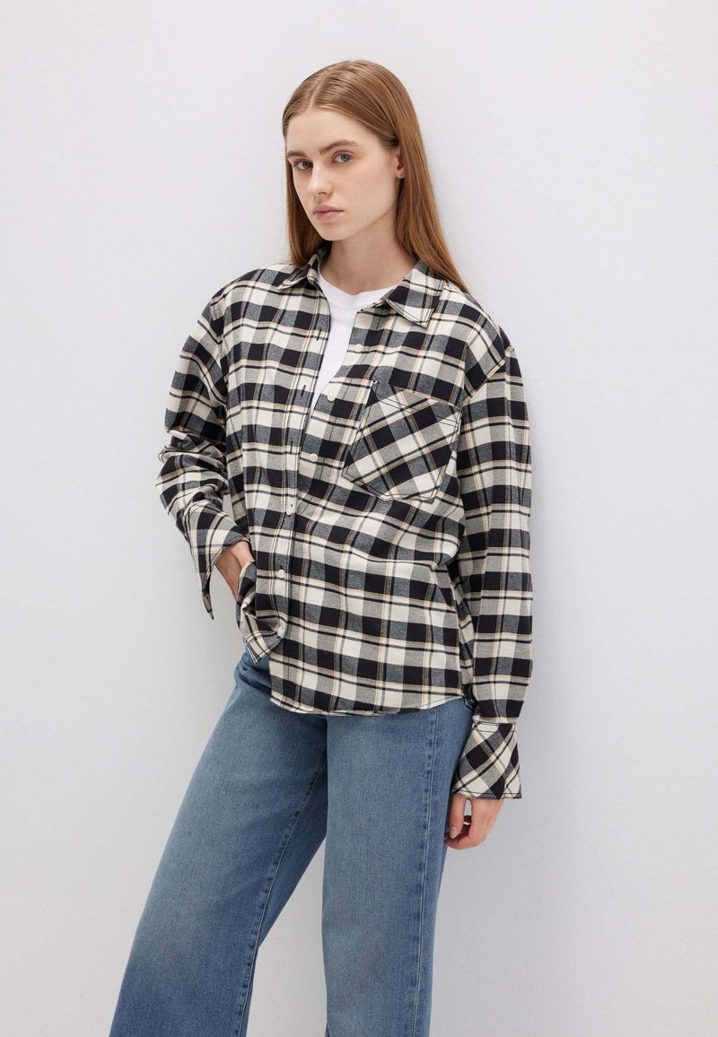 Camicia a quadri bianca e nera con maniche lunghe, chiusura bottonata davanti e un'unica tasca sul petto; abbinata a jeans in denim azzurro chiaro.