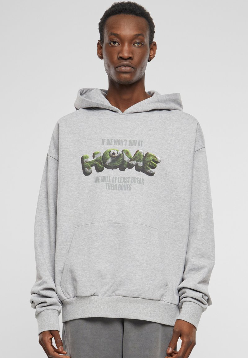 Sweatshirt à capuche gris avec une poche avant, présentant un design de texte graphique en vert et noir portant l'inscription "HOME" et des phrases accompagnantes.