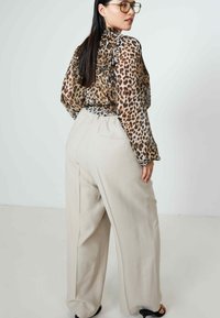 Transparante blouse met luipaardprint en een gathered halslijn, gecombineerd met losse, lichtbeige broek. Gladde stof, subtiele glans, wijde pijp silhouet.