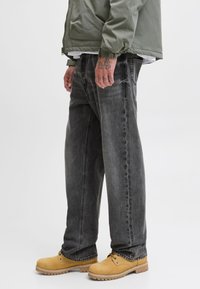 Szare dżinsy o szerokich nogawkach z efektem sprania, połączone z żółtymi butami roboczymi. Dopełnieniem stroju jest zielona kurtka i biała koszulka pod spodem.