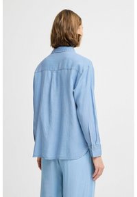 Camicia di denim blu chiaro con maniche lunghe e colletto con bottoni, caratterizzata da una vestibilità rilassata e orlo curvo. Texture morbida con dettagli di cucitura discreti.