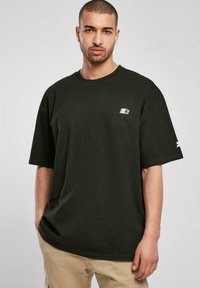 Black oversized t-shirt made of cotton. Features a small white logo on the left chest and a design on the sleeve. Short sleeves.