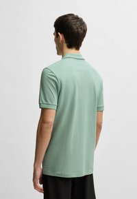 Mint green polo shirt with a collar and short sleeves, featuring a smooth texture and a straight hemline. Simple and modern design.