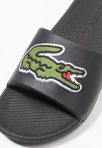 Sandale noire à glissière avec semelle intérieure texturée et logo crocodile brodé vert sur la bride.