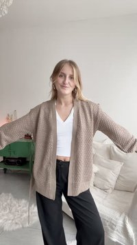 Beżowy kardigan o fakturze z luźnym krojem, długimi rękawami i otwartym przodem. Noszony na biały top i zestawiony z czarnymi spodniami.