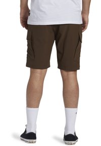 Hnědé cargo šortky s dvojitými bočními kapsami, s plochým předním dílem a elastickým pasem, doplněné o bílé ponožky a černé sneakers.