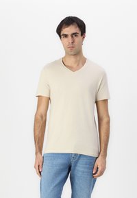 Beige V-Ausschnitt-T-Shirt aus weichem Stoff, mit kurzen Ärmeln und figurnahen Schnitt. Das Design ist schlicht ohne Muster oder Verzierungen.