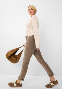 Beiger gestrickter Pullover, taupefarbene Cordhose und braune Wildledersneaker mit weißen Akzenten. Braune, lässige Tasche mit Nieten.