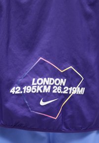 Μοβ ύφασμα με λευκό κείμενο "LONDON 42.195KM 26.219MI" μέσα σε περίγραμμα ακανόνιστου πολύγωνου, συνοδευόμενο από λευκό λογότυπο Nike swoosh από κάτω.