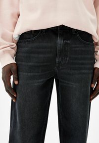 Tummansiniset farkut suoralla leikkauksella, joissa näkyvät saumat, viisi taskua ja vyötärökaitteen reunasta pilkottava merkki. Teksturoitu kangas.