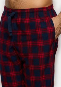 Czerwono-granatowe spodnie piżamowe w kratę, wykonane z miękkiego materiału, z elastycznym paskiem w talii oraz sznurkiem, a także bocznymi kieszeniami.