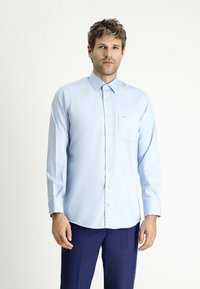 Camicia azzurra chiara a maniche lunghe con chiusura a bottoni e taschino sul petto. Vestibilità tailored, texture liscia e colletto appuntito. I bottoni sono bianchi.