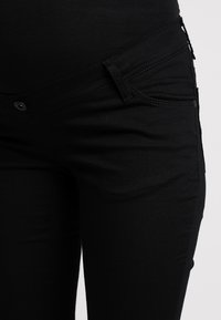 Calças jeans pretas feitas de tecido suave, com um design ajustado, bolsos frontais e fecho de botão com detalhes de costura contrastante.