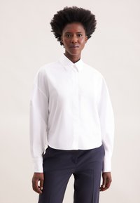Camicia bianca oversized con colletto a punta e chiusura con bottoni sul davanti, caratterizzata da maniche lunghe e una texture in cotone liscia.