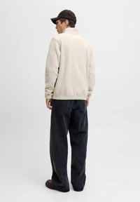 Beige fleece jacket with a high collar, paired with loose black jeans. The design features a relaxed fit and minimal detailing.