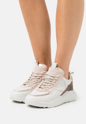 Ben met witte chunky sneakers met roze suède en getextureerde bruine accenten op een witte achtergrond.