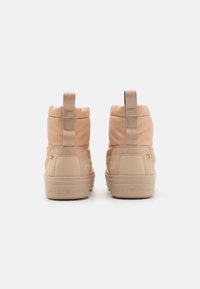 Beige enkellaarsjes met een bovenwerk van gewatteerde stof, rubberen zool en een trekhaak aan de achterkant. Voorzien van subtiele branding op de hak en gestructureerde accenten.