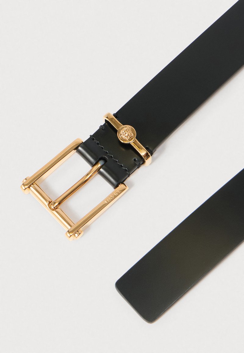Black leather belt with a gold-tone metal buckle, featuring a double prong and logo detail. Smooth finish, flat shape, and straight edges.