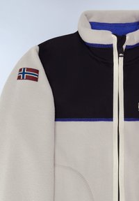 Fleecejacka med en svart övre del, ljusgrå nedre del, blå sömmar och ett märke med den isländska flaggan på ärmen.