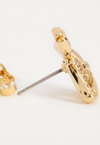 Pendiente de botón de oro con diseño detallado de corona y cierre de mariposa extraíble sobre un fondo blanco.