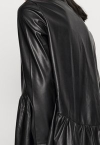 Svart läderjacka med en slät yta, en åtsittande överdel och en ryschad peplumdetalj vid midjan.