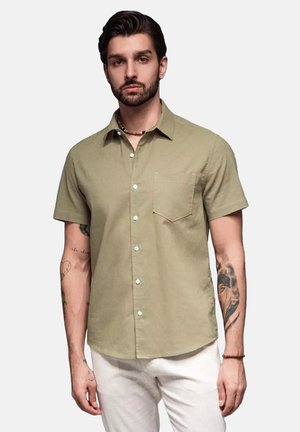 Chemise à manches courtes, d'un vert olive clair, à boutons, confectionnée dans un tissu doux, avec une poche sur la poitrine et des boutons blancs.