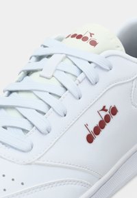 Λευκό δερμάτινο αθλητικό παπούτσι με γαλάζια κορδόνια και γλώσσα σε μέντα πράσινο χρώμα. Διακριτικό κόκκινο λογότυπο και πλευρικές λεπτομέρειες με διάτρητα στοιχεία.