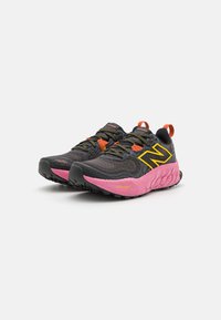 Scarpe da corsa nere e rosa con tomaia in rete, lacci arancioni, logo giallo e suola testurizzata. Presentano una tecnologia di ammortizzazione e un design robusto.