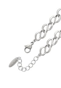 Strieborný náramok z retiazky s veľkými oválnymi článkami, s karabínovým zapínaním a oválnou visačkou s vygravírovanými iniciálami značky. Hladký, lesklý povrch.