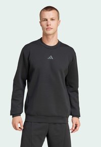 Black sweatshirt made of soft material, featuring a crew neckline, long sleeves, and a small gray logo on the chest. Fitted design.
