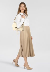 Borsa color crema con chiusura a patta e dettagli in oro, abbinata a una camicia bianca con bottoni e a una gonna beige a pieghe, indossata con scarpe con tacco color nude.