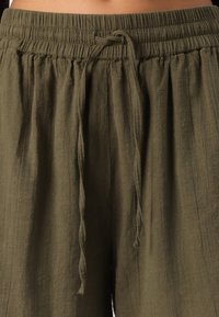 Pantalons texturés légers de couleur vert olive, avec une taille élastique et un cordon de serrage ajustable. Caractéristiques d'un tissu ample et fluide.