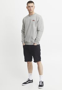 Gray sweatshirt with a small multicolored rainbow logo, paired with black rolled shorts and black sneakers. Background is plain white.