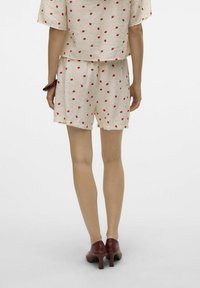 Lichtbeige outfit met rode stippen, inclusief een losse top en bijpassende shorts. Geraadpleegd met bordeauxrode hakken, met een gladde textuur.