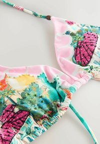 Bikini felső rózsaszín, zöld és türkiz trópusi mintával, apró gyöngyökkel díszítve, és sokszínű, ráncolt pántokkal, semleges háttéren.