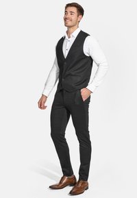 Grau texturieste Weste über einem weißen Hemd, kombiniert mit schmal geschnittenen grauen Hosen und braunen Lederschuhen mit dekorativen Perforationen.