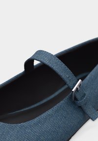 Chaussure Mary Jane en tissu bleu avec une boucle argentée sur la bride ajustable et une doublure intérieure noire.