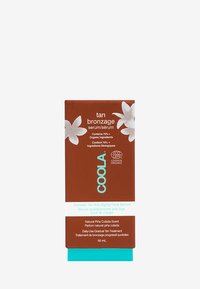 Coola Sunless Tan Anti-Aging Serum in einer braunen Schachtel mit weißen floralen Grafiken; hat einen türkisfarbenen Boden und Text in Weiß und Hellblau.