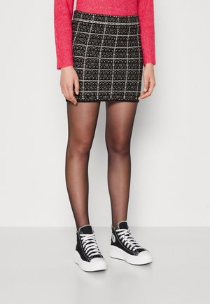 Femme portant un pull rose, une mini-jupe à carreaux noir et blanc, des collants noirs transparents et des baskets montantes noires avec des semelles blanches.