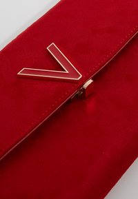 Punainen mokkalaukku, jossa edessä kiiltävä punainen kulmikas metallikoriste, vetoketjusuljenta piilotettu ja siistit ompeleet.