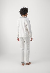 Långärmad, vit pyjamasset gjort av mjukt material, med svarta kantband på kragen och ärmsluten; avslappnade byxor med raka ben.