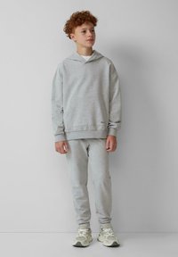 Grijze sweatshirt en sweatpants set van zachte stof. Met een capuchon en een voorzak. Model draagt lichte sneakers. Eenvoudig kleurenpalet.