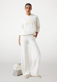 Witte hoodie met reliëf "GUESS" logo, gecombineerd met bijpassende wijduitlopende broek. Inclusief een bicolor grijs en witte handtas. Glad materiaal.