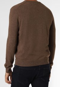 Brauner Strickpullover mit langen Ärmeln, rundem Hals und gerippten Bündchen. Weiche Textur, taillierte Form, getragen über dunkler Jeans.
