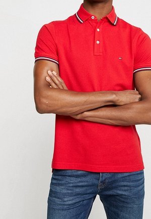 Rotes Polohemd mit Kragen, ausgestattet mit einer Zwei-Knopf-Leiste und marineblauen sowie weißen gestreiften Akzenten am Kragen und den Ärmeln. Aus Baumwolle.