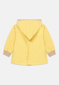 Κίτρινο αδιάβροχο μπουφάν με κουκούλα, μπεζ ριμπ μανσέτες και ίσια γραμμή. Λεπτή υφή, ελάχιστες λεπτομέρειες και χωρίς ορατά κουμπώματα.