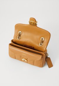 Tan leather handbag with quilted pattern, gold-tone hardware, and dual compartments. Interior features a card slot and a detachable tag.