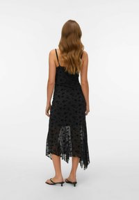 Černé květinové šaty s průsvitným překryvem, tenkými ramínky a asymetrickým lemem, s propracovanými květinovými vzory a splývavým siluetou.