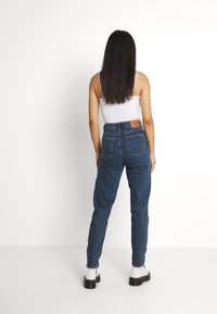 Vaaleat korkeavyötäröiset siniset farkut, joissa on takatasku ja kapenevat lahkeet, yhdistettynä vartalonmyötäiseen valkoiseen hihattomaan puseroon ja mustiin korokepolkimiin.