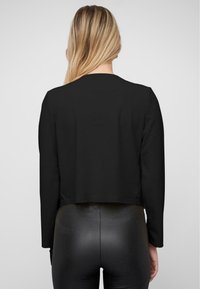 Must värvitud lühikeste varrukatega topp, mis on valmistatud siledast kangast. Minimalistlik disain ümmarguse kaelusega ja ilma nähtavate kinnitusteta.